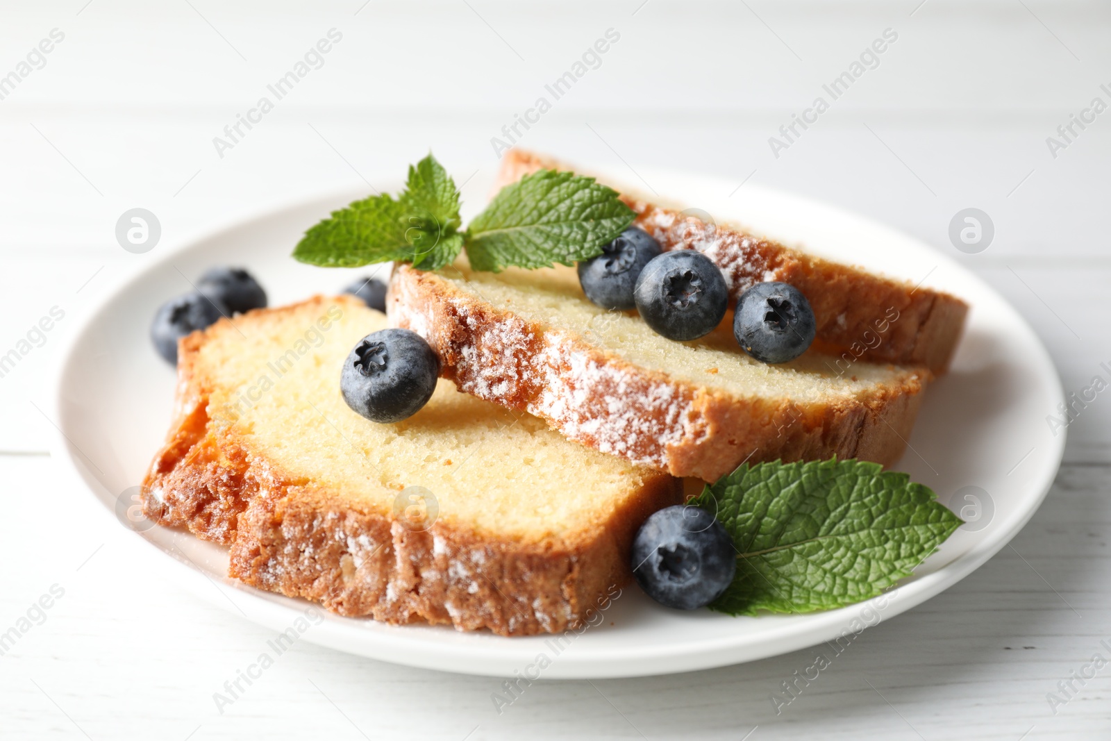 Photo of Freshly baked sponge cake, mint and blueberries on white wooden table