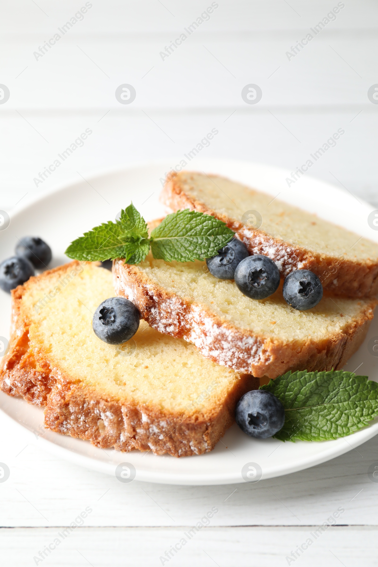 Photo of Freshly baked sponge cake, mint and blueberries on white wooden table