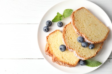 Photo of Freshly baked sponge cake, mint and blueberries on white wooden table, top view