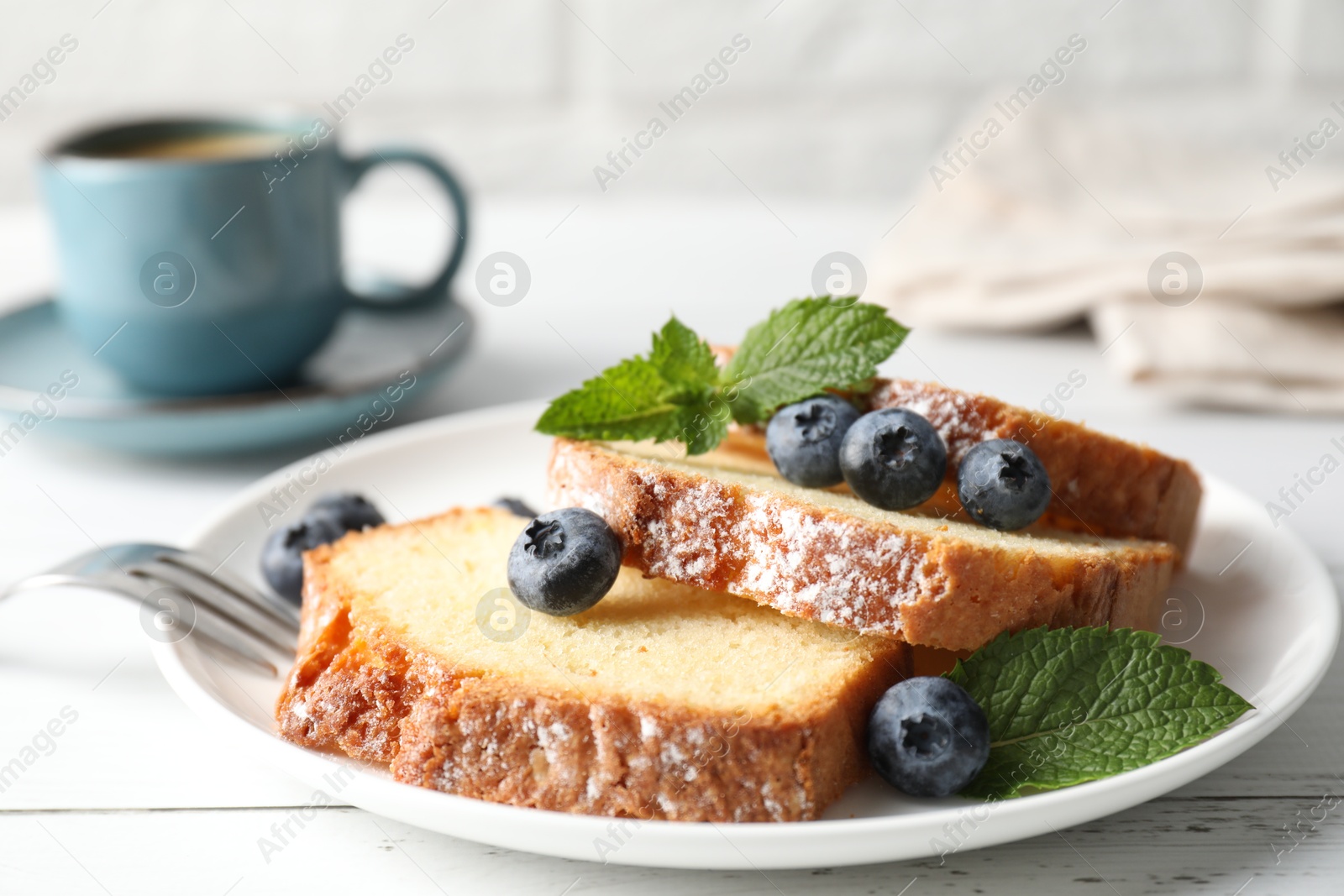 Photo of Freshly baked sponge cake, mint and blueberries on white wooden table, closeup