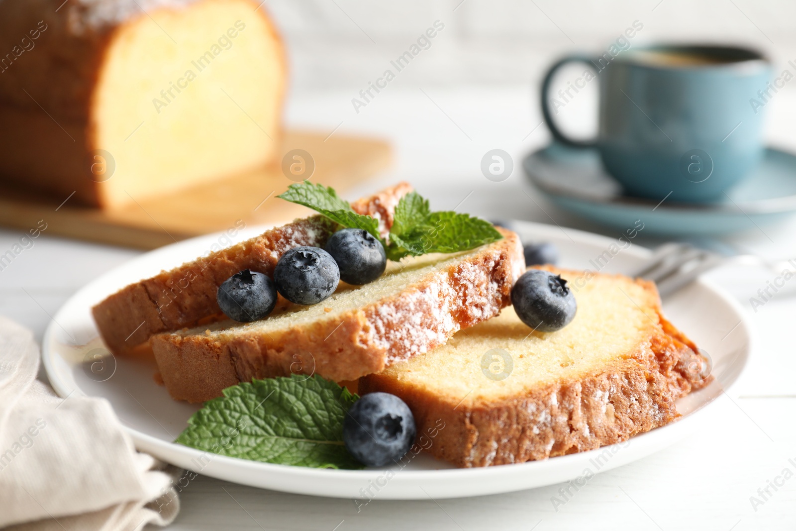 Photo of Freshly baked sponge cake, mint and blueberries on white wooden table, closeup