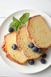 Photo of Freshly baked sponge cake, mint and blueberries on white wooden table, top view