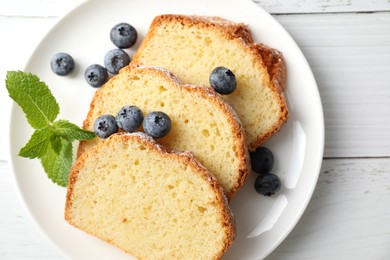 Photo of Freshly baked sponge cake, mint and blueberries on white wooden table, top view