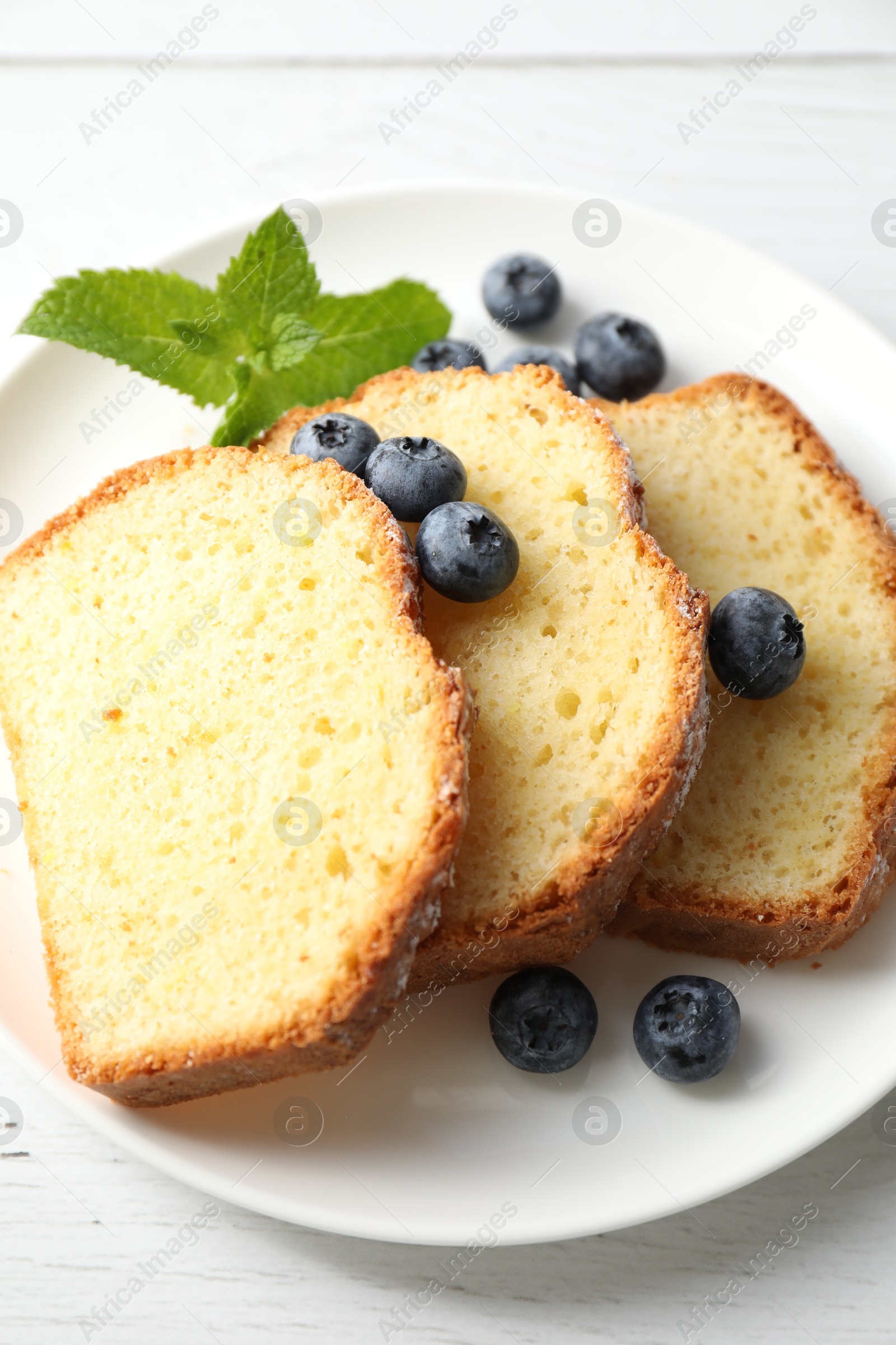 Photo of Freshly baked sponge cake, mint and blueberries on white wooden table, closeup