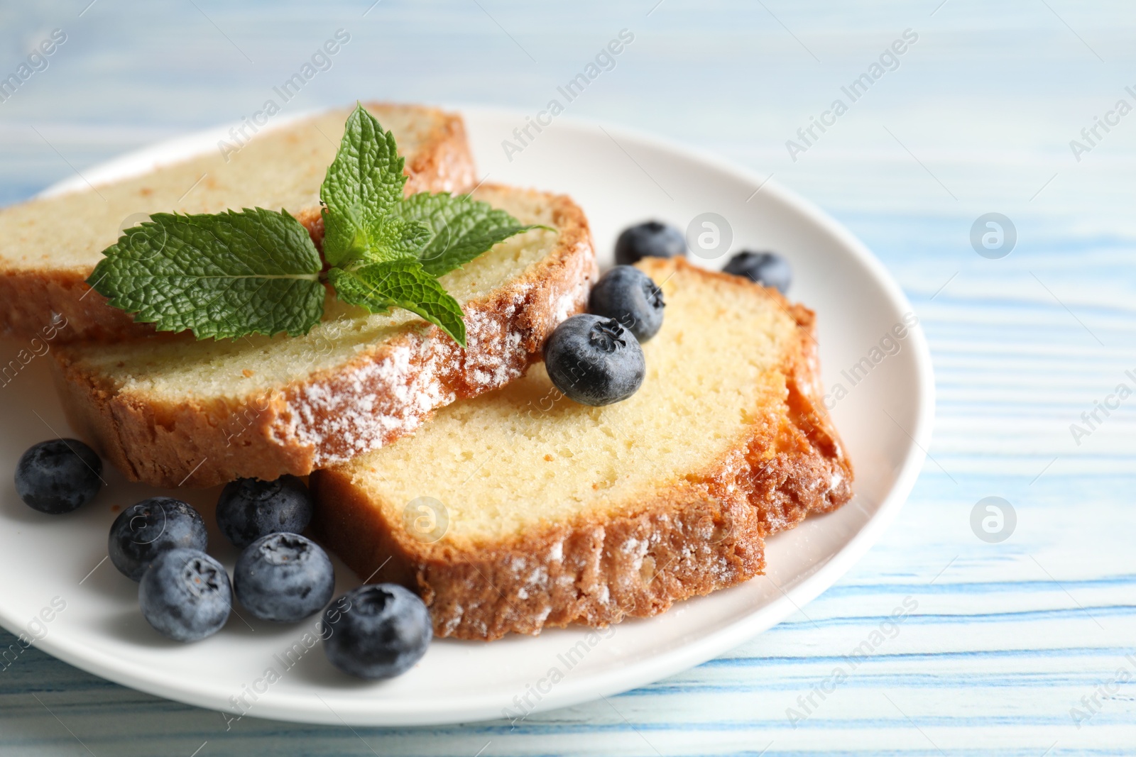 Photo of Freshly baked sponge cake, blueberries and mint on light blue wooden table, closeup