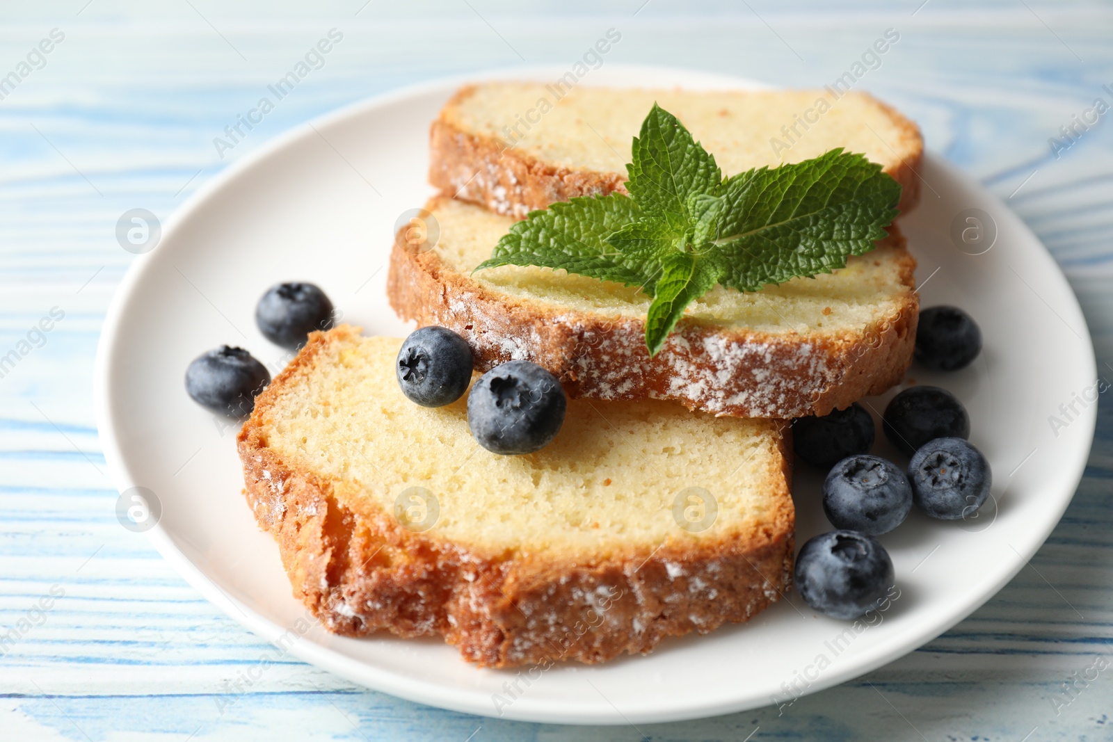 Photo of Freshly baked sponge cake, blueberries and mint on light blue wooden table, closeup