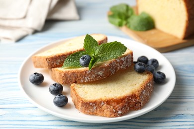 Photo of Freshly baked sponge cake, blueberries and mint on light blue wooden table, closeup