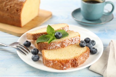 Photo of Freshly baked sponge cake, blueberries and mint on light blue wooden table, closeup