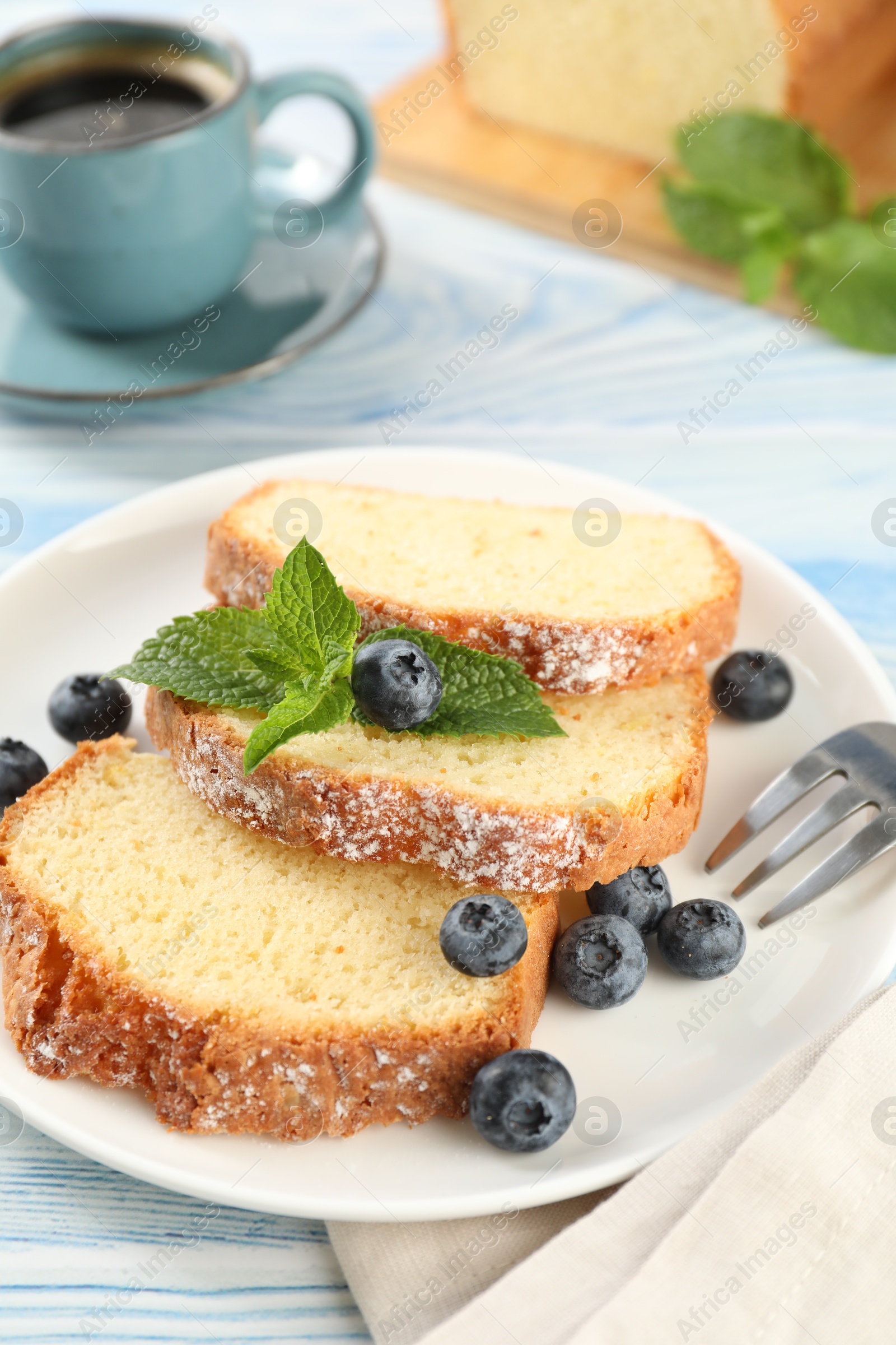 Photo of Freshly baked sponge cake, blueberries and mint on light blue wooden table, closeup