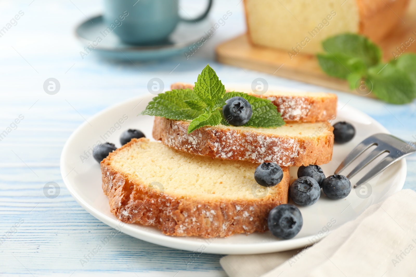 Photo of Freshly baked sponge cake, blueberries and mint on light blue wooden table, closeup