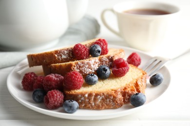 Photo of Freshly baked sponge cake, raspberries and blueberries on white wooden table, closeup