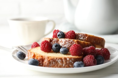 Photo of Freshly baked sponge cake, raspberries and blueberries on white wooden table, closeup