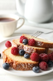 Photo of Freshly baked sponge cake, raspberries and blueberries on white wooden table, closeup