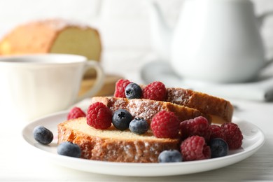 Photo of Freshly baked sponge cake, raspberries and blueberries on white wooden table, closeup