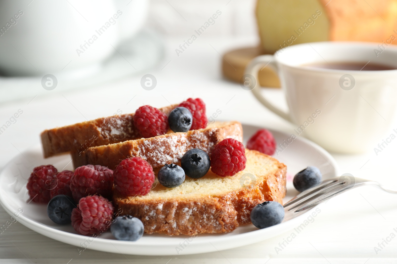 Photo of Freshly baked sponge cake, raspberries and blueberries on white wooden table, closeup