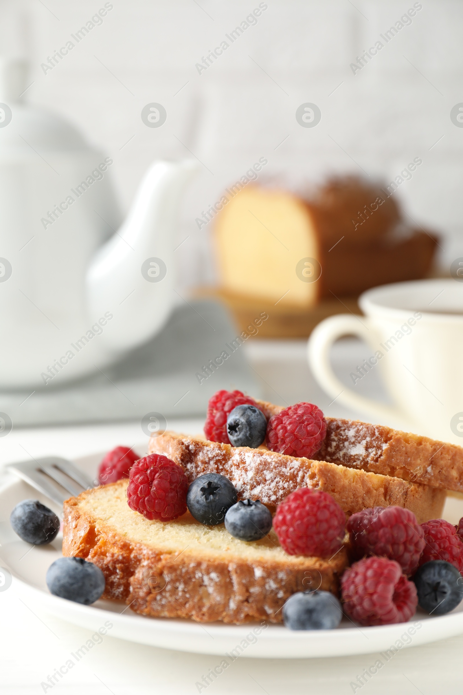 Photo of Freshly baked sponge cake, raspberries and blueberries on white wooden table, closeup