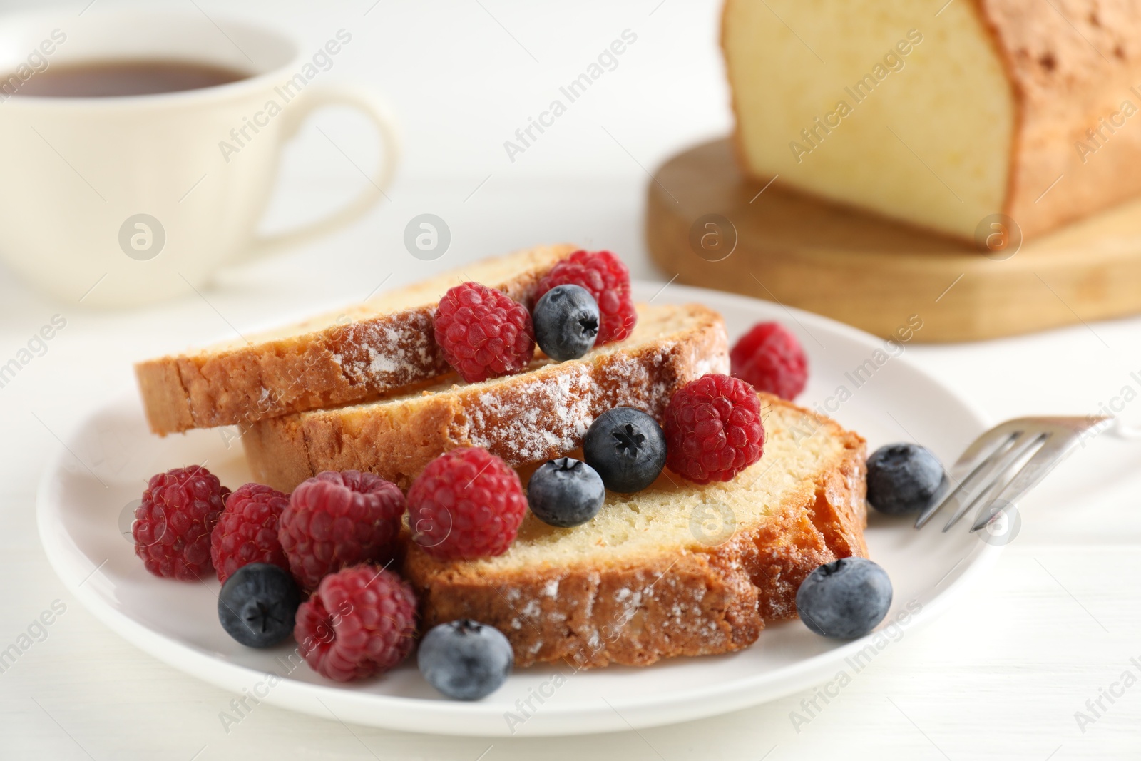 Photo of Freshly baked sponge cake, raspberries and blueberries on white wooden table, closeup