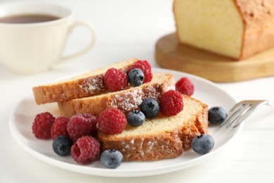 Photo of Freshly baked sponge cake, raspberries and blueberries on white wooden table, closeup