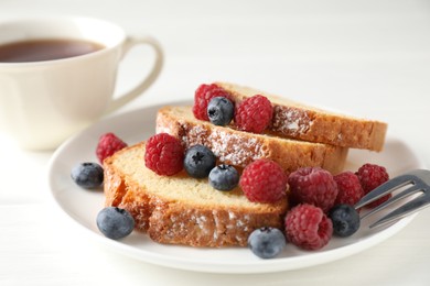 Photo of Freshly baked sponge cake, raspberries and blueberries on white wooden table, closeup