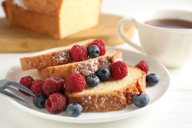 Photo of Freshly baked sponge cake, raspberries and blueberries on white wooden table, closeup