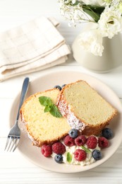 Photo of Freshly baked sponge cake, whipped cream, berries and mint on white wooden table