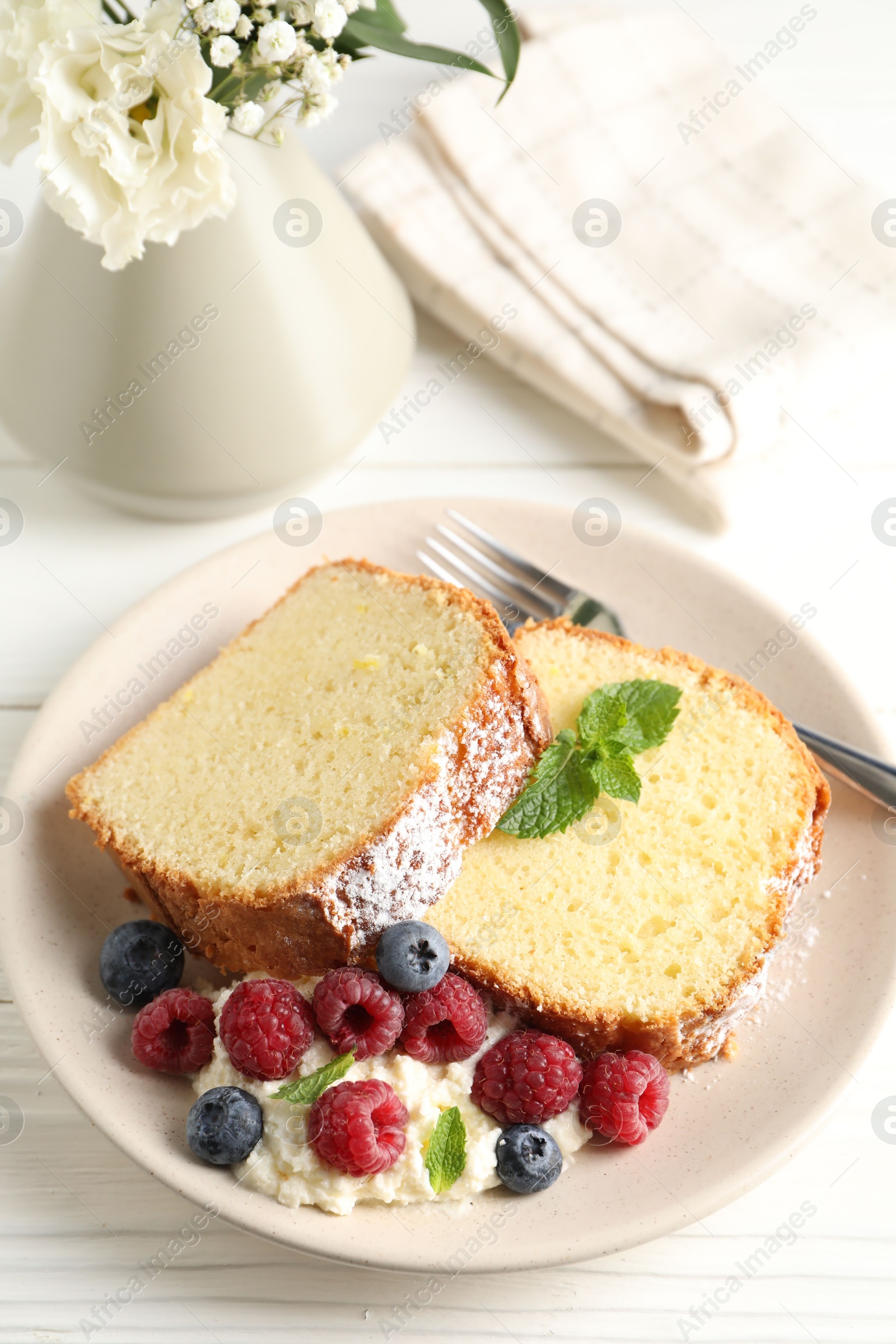 Photo of Freshly baked sponge cake, whipped cream, berries and mint on white wooden table