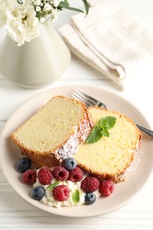 Photo of Freshly baked sponge cake, whipped cream, berries and mint on white wooden table