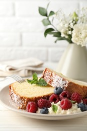 Photo of Freshly baked sponge cake, whipped cream, berries and mint on white wooden table, closeup