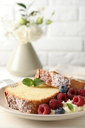 Photo of Freshly baked sponge cake, whipped cream, berries and mint on white wooden table, closeup