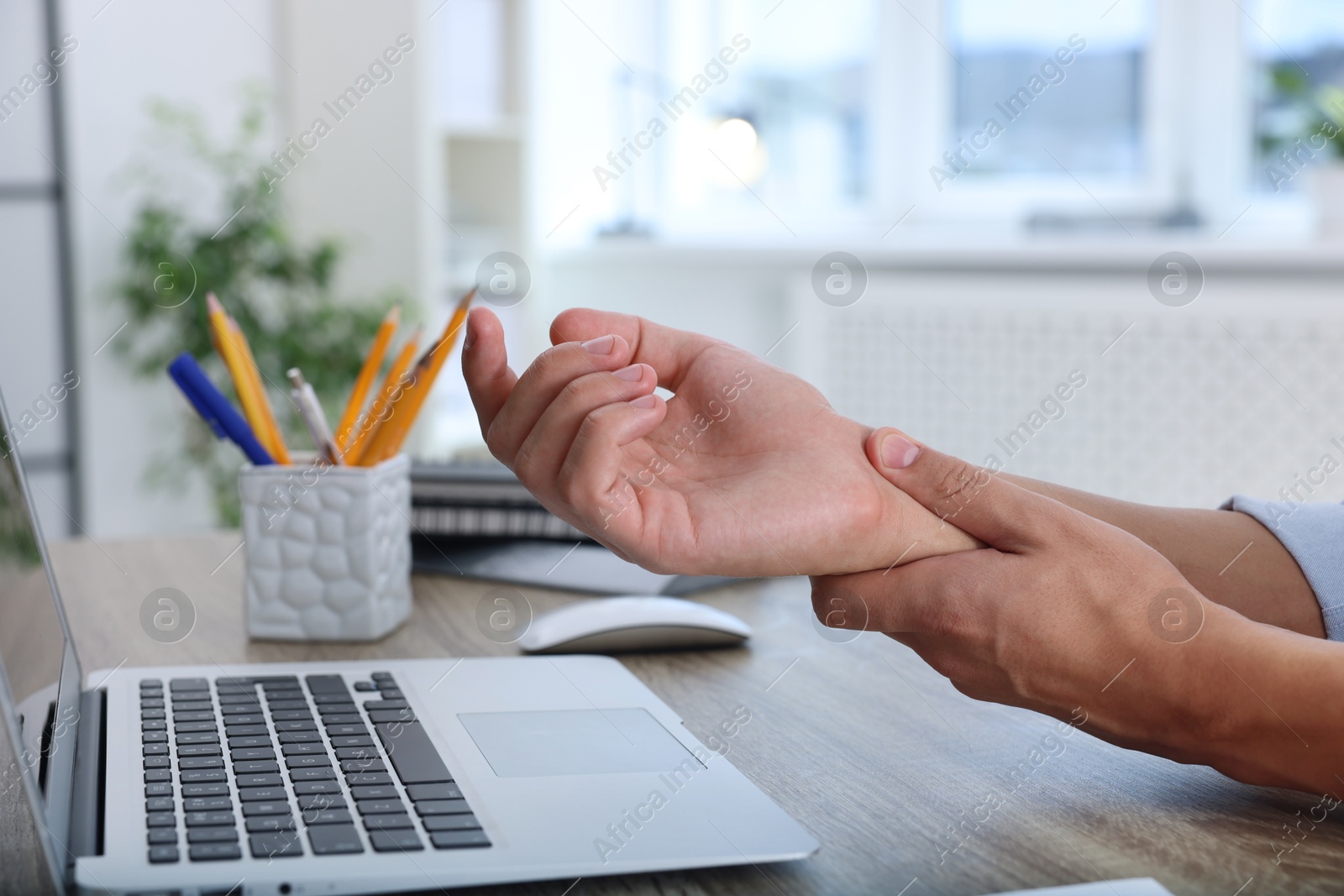 Photo of Man suffering from pain in wrist while working on laptop at table indoors, closeup. Carpal tunnel syndrome