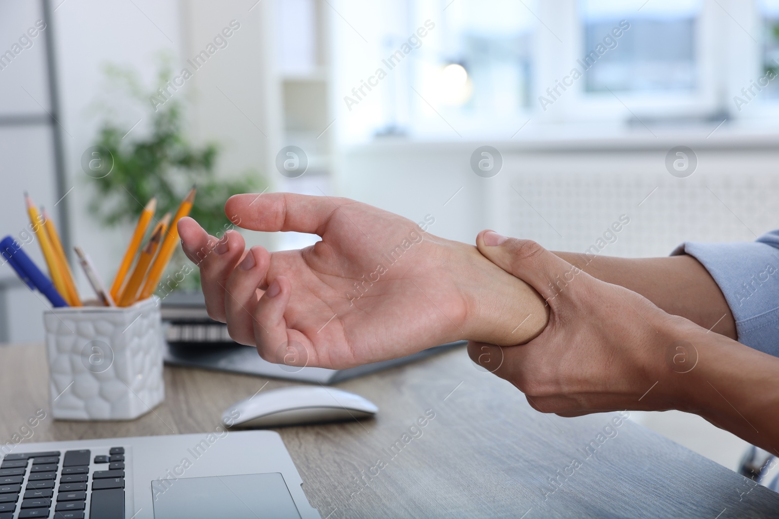 Photo of Man suffering from pain in wrist while working on laptop at table indoors, closeup. Carpal tunnel syndrome