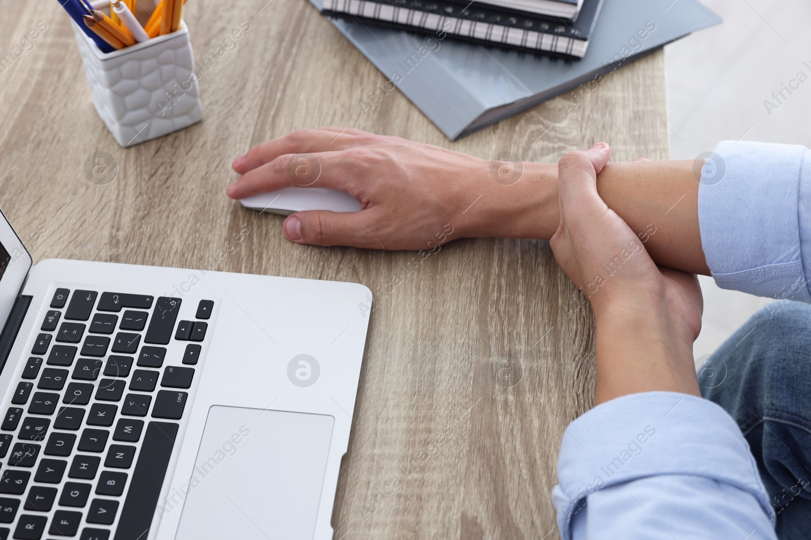 Photo of Man suffering from pain in wrist while using computer mouse at wooden table, closeup. Carpal tunnel syndrome