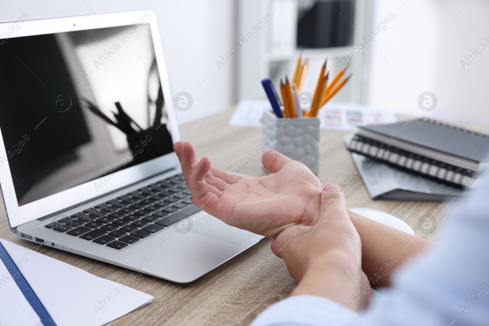 Photo of Man suffering from pain in wrist while working on laptop at table indoors, closeup. Carpal tunnel syndrome