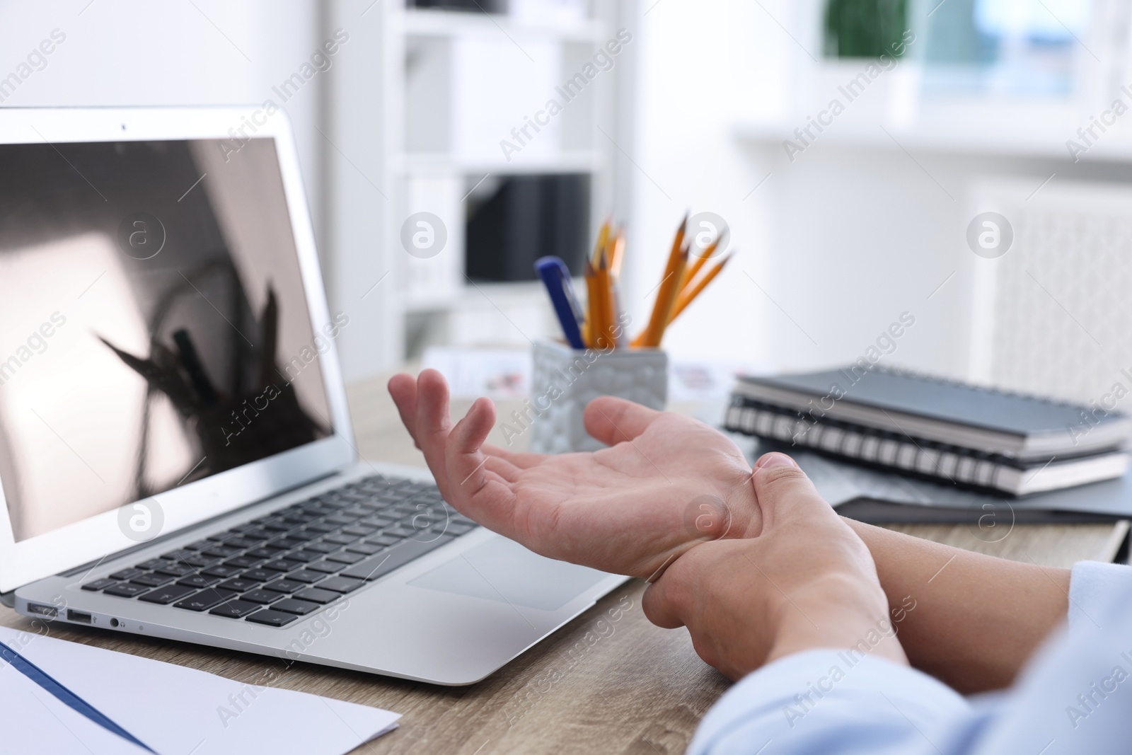 Photo of Man suffering from pain in wrist while working on laptop at table indoors, closeup. Carpal tunnel syndrome