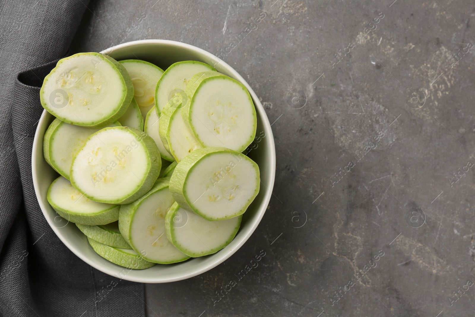 Photo of Fresh cut zucchinis in bowl on grey textured table, top view. Space for text