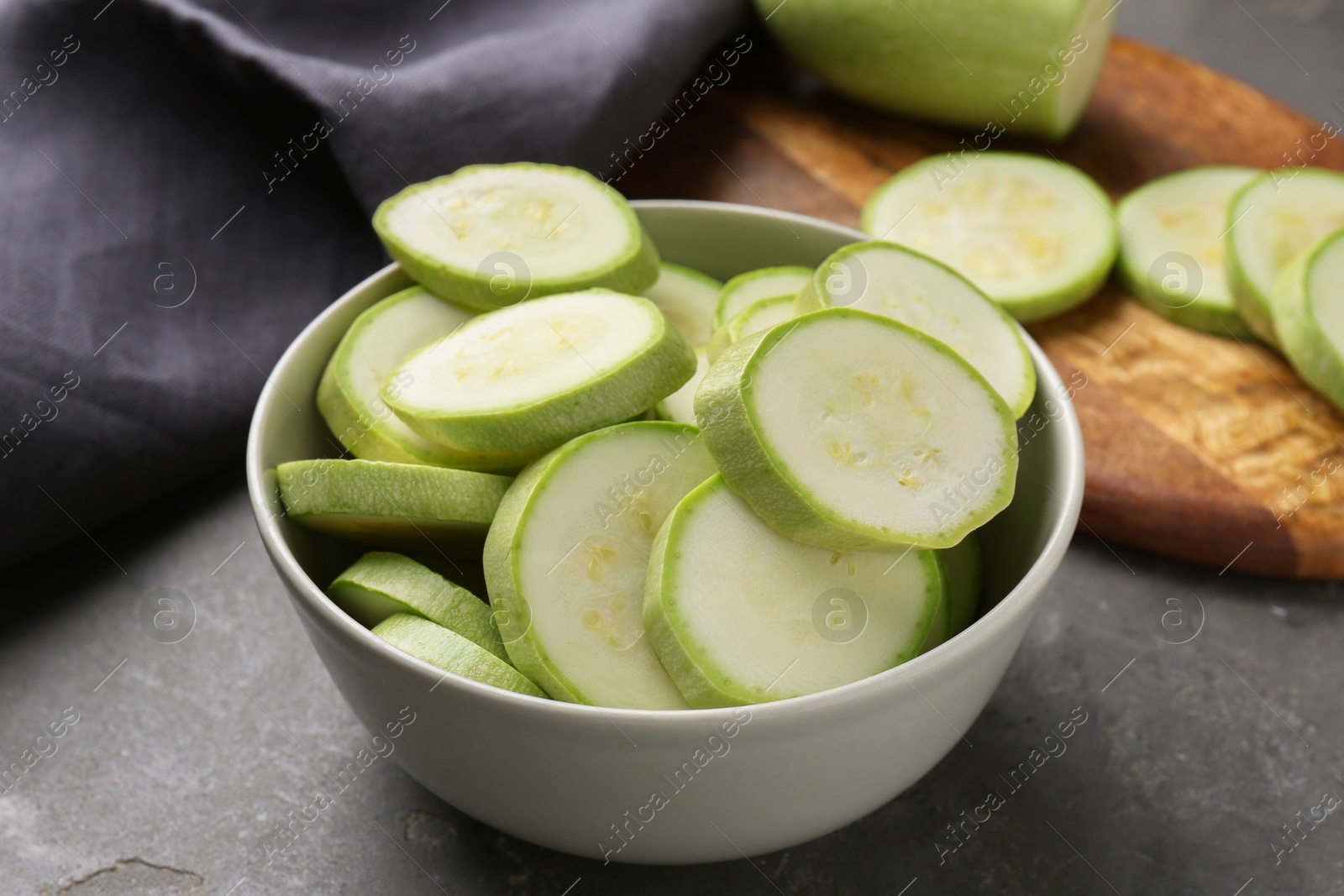 Photo of Fresh cut zucchinis in bowl on grey textured table, closeup