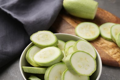 Photo of Fresh cut zucchinis in bowl on grey textured table, closeup