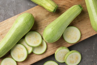 Photo of Board with fresh cut and whole zucchinis on grey textured table, flat lay