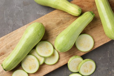 Photo of Board with fresh cut and whole zucchinis on grey textured table, flat lay