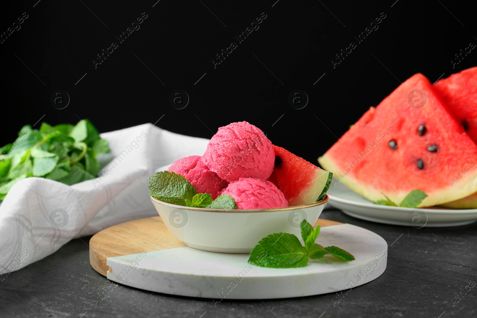 Photo of Scoops of tasty watermelon sorbet with mint and fresh fruit in bowl on grey textured table