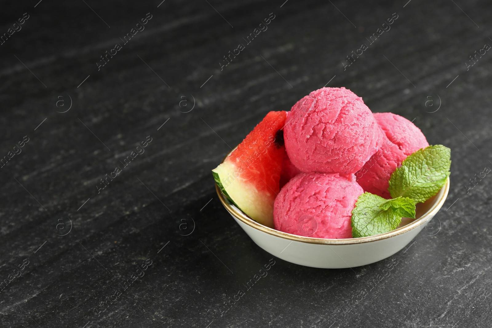 Photo of Scoops of tasty watermelon sorbet with mint and fresh fruit in bowl on grey textured table, space for text