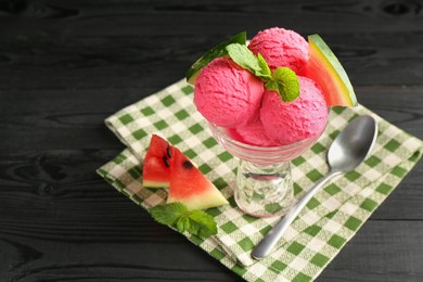 Photo of Scoops of tasty watermelon sorbet in glass dessert bowl with fresh fruit and spoon on black wooden table