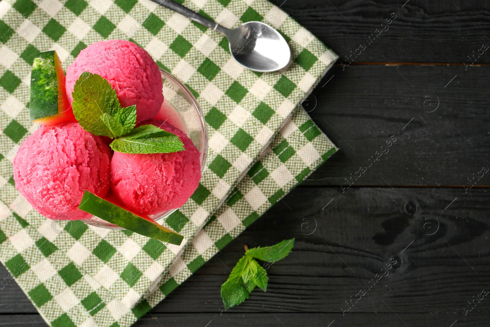 Photo of Scoops of tasty watermelon sorbet in glass dessert bowl with fresh fruit and spoon on black wooden table, flat lay. Space for text