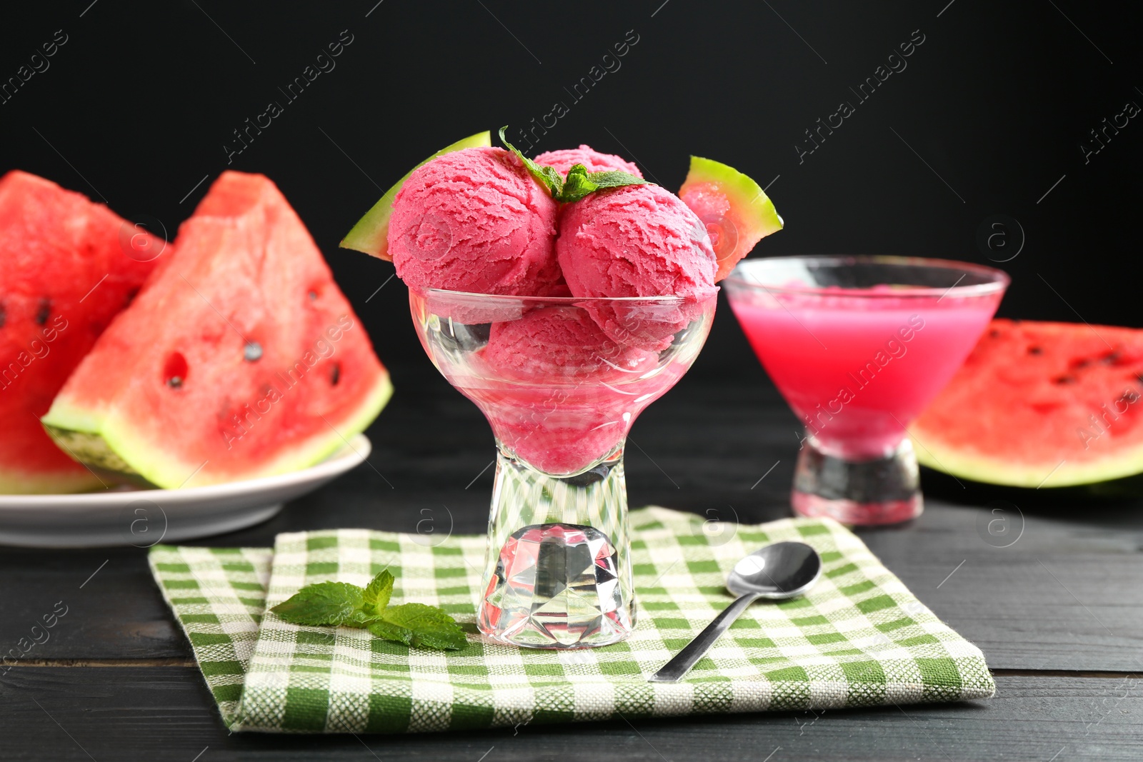 Photo of Scoops of tasty watermelon sorbet with mint, fresh fruit in glass dessert bowl and spoon on wooden table