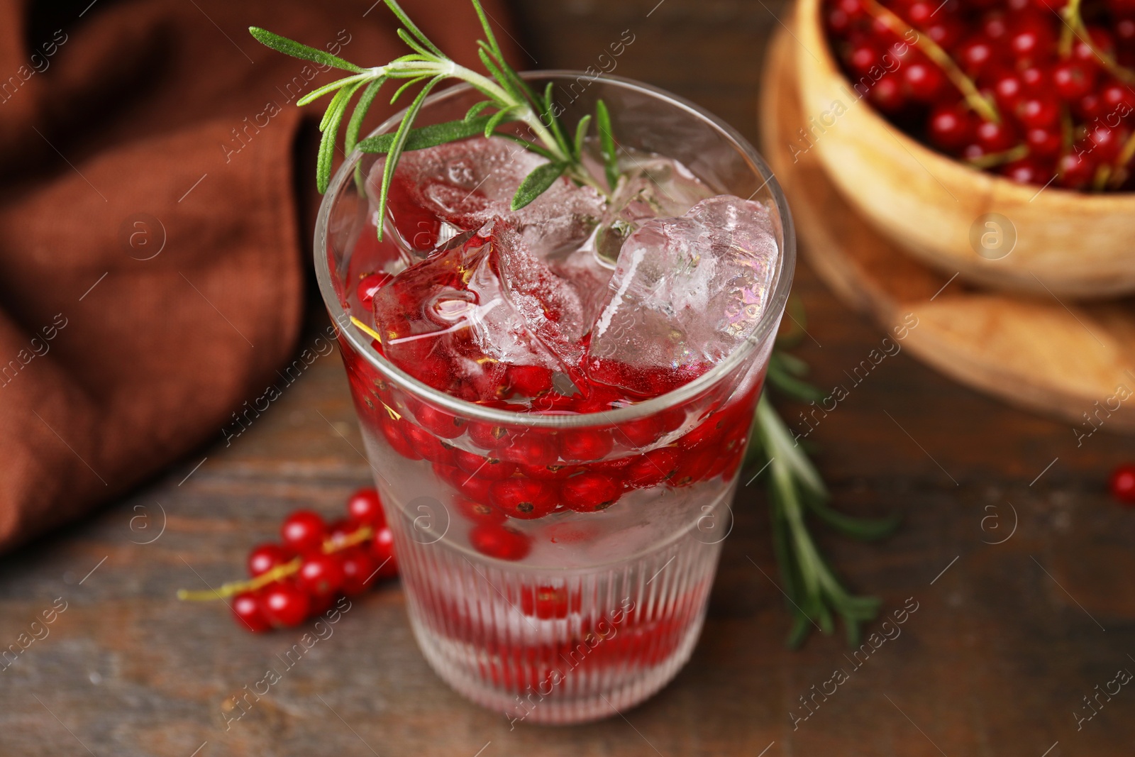 Photo of Refreshing water with red currants and rosemary in glass on wooden table, closeup