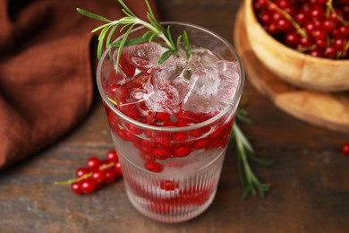 Photo of Refreshing water with red currants and rosemary in glass on wooden table, closeup