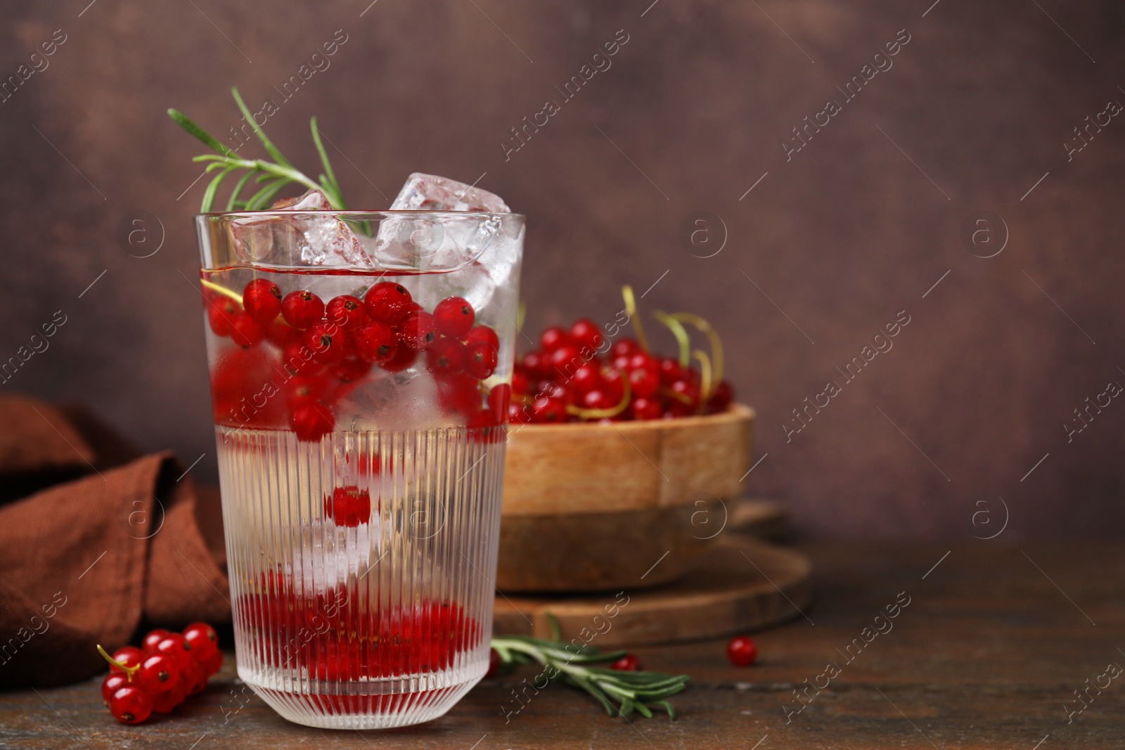 Photo of Refreshing water with red currants and rosemary in glass on wooden table, space for text