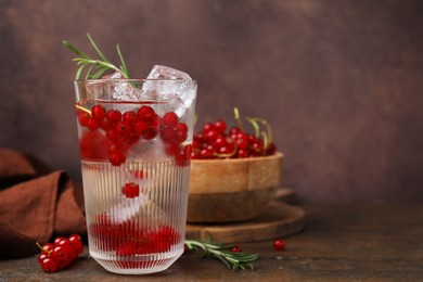 Photo of Refreshing water with red currants and rosemary in glass on wooden table, space for text