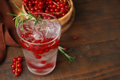 Photo of Refreshing water with red currants and rosemary in glass on wooden table, closeup. Space for text