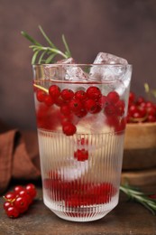 Photo of Refreshing water with red currants and rosemary in glass on wooden table, closeup